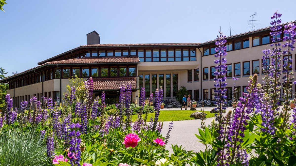 Ansicht des Haupteingangs der Klinik Alpenblick mit überdachtem Eingangsbereich und Blumen im Vordergrund