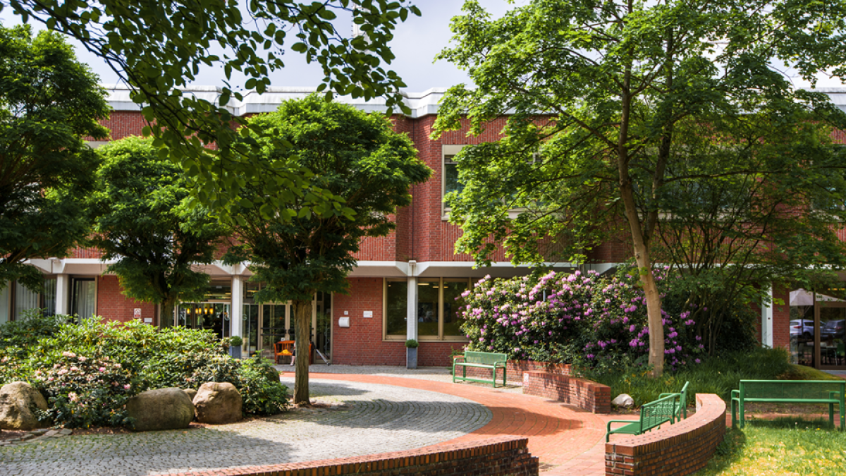 Außenansicht der Reha Klinik am Sendesaal mit Rondell, Sitzbänken und Bäumen