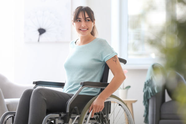 Eine Frau im Rollstuhl fährt selbstbewusst durch ihr Wohnzimmer und blickt zuversichtlich in den Raum.