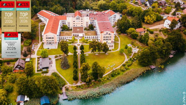 uftaufnahme der Fachklinik Feldberg – Klinik am See mit weitläufigem Gebäude, gepflegter Parkanlage und direkter Lage am Ufer eines Sees, umgeben von Bäumen und Wohnhäusern.