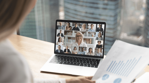 Laptop mit Videokonferenz mehrerer Teilnehmender, im Vordergrund liegt ein Dokument mit Diagrammen.