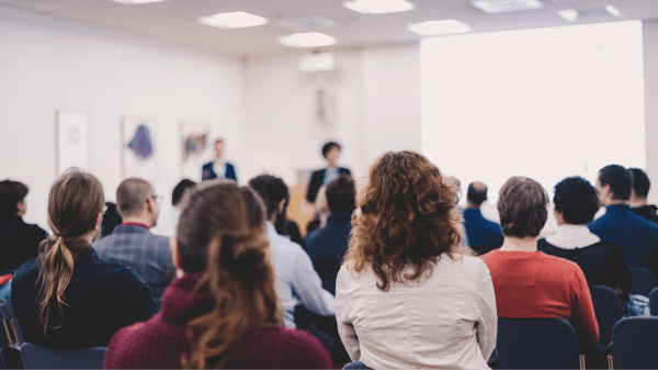 Teilnehmende bei einer Fachkonferenz, Vortragende präsentiert Inhalte vor großem Publikum.