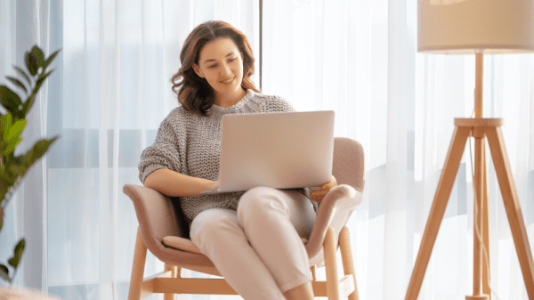 Eine Frau sitzt in einem hellen Wohnzimmer auf einem Stuhl vor einem Laptop und recherchiert online nach Gesundheitsinformationen.