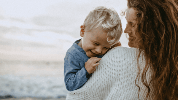 Mutter mit Kind auf dem Arm am Strand.