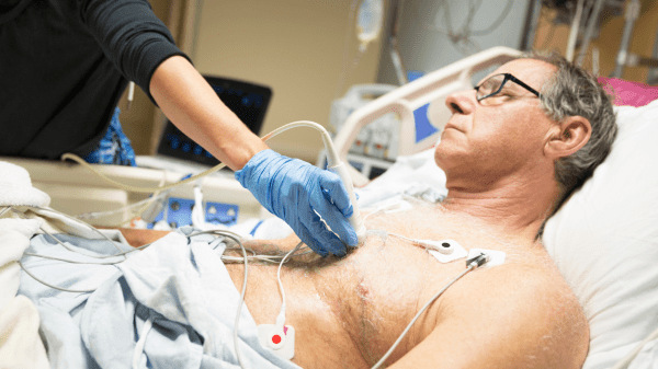 Ein stabiler, schwer verletzter Patient liegt auf einer Überwachungsstation und wird medizinisch betreut. Die Szene zeigt eine postakute Phase vor der regulären Rehabilitation.