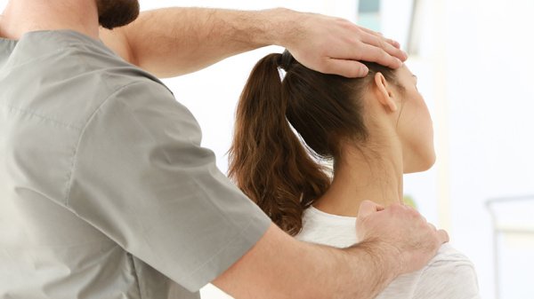 Therapeut untersucht den Nackenbereich einer Patientin nach einer Operation der Halswirbelsäule.