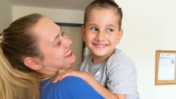 Pflegerin hält lächelnd einen kleinen Patienten im Arm – einfühlsame Betreuung in der VAMED Rehaklinik Altona