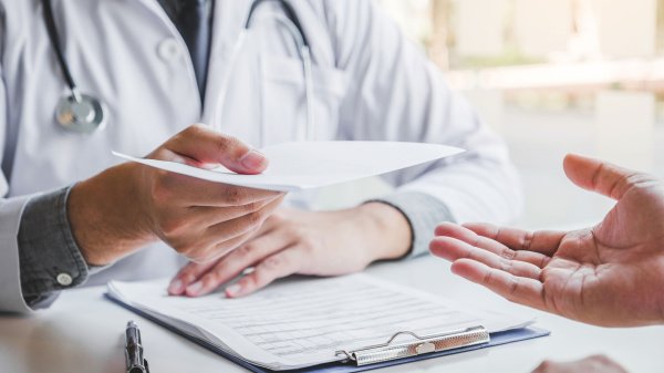 Arzt übergibt Unterlagen an einen Patienten zur Beantragung einer Reha-Verlängerung.
