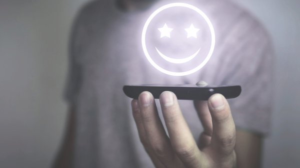 Hand hält Smartphone mit leuchtendem Smiley: Symbol für digitalen Service und Kundenzufriedenheit.