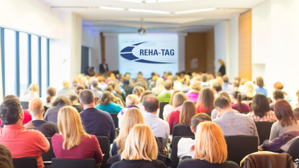 Veranstaltungsteilnehmer sitzen mit Blick auf Leinwand, Logo des Deutschen Reha-Tags auf der Leinwand
