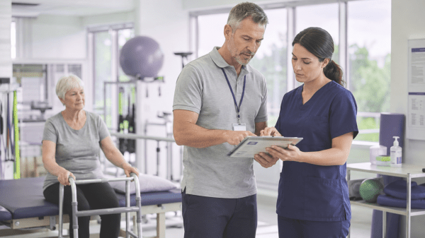 Gesundheitsfachkräfte prüfen in Reha-Einrichtung Therapieplan. Patientin mit Gehhilfe wartet.