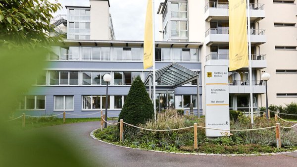 Außenansicht des Haupteingangs der Rehabilitationsklinik Bad Wurzach – moderne Architektur inmitten grüner Umgebung, mit gut erkennbarer Beschilderung und barrierefreiem Zugang.