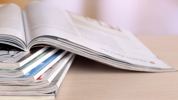 Aufgeschlagene Fachzeitschrift auf einem Stapel Printmagazine, auf hellem Holztisch – Symbolbild für Veröffentlichung in f&w