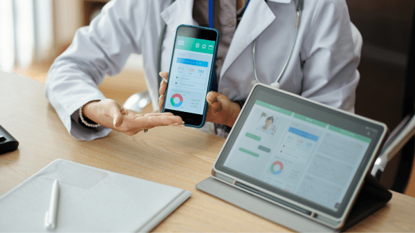 Eine medizinisches Fachperson, die ein Handy hält. Neben ihr ein Tablet. Darauf sind mehrere Grafiken und Kennzahlen zu sehen