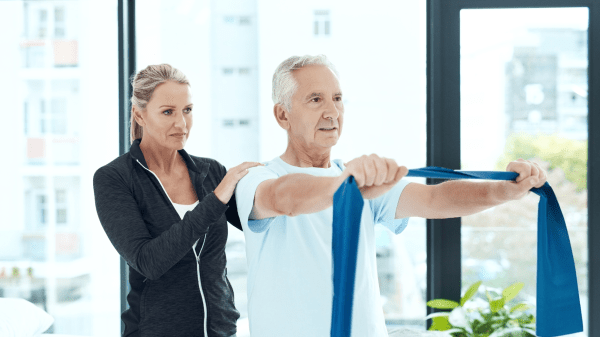 Therapeutin begleitet Patienten bei Übung mit Theraband im Rahmen der medizinischen Rehabilitation