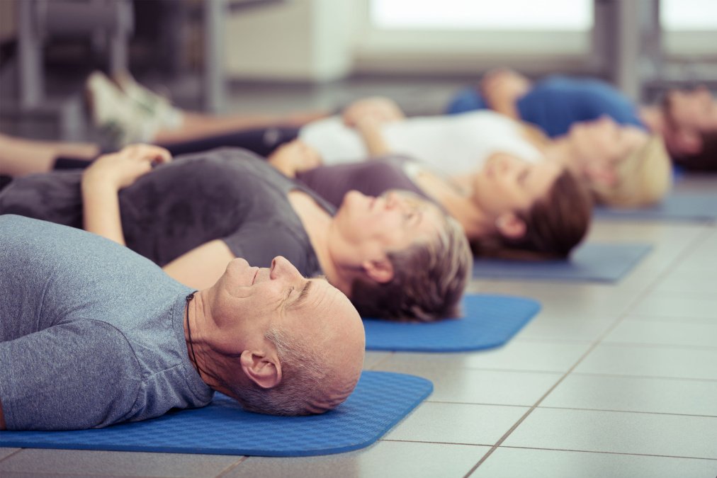 Menschen liegen entspannt auf Gymnastikmatten. Symbolbild zu Unterschieden zwischen Reha und Kur.