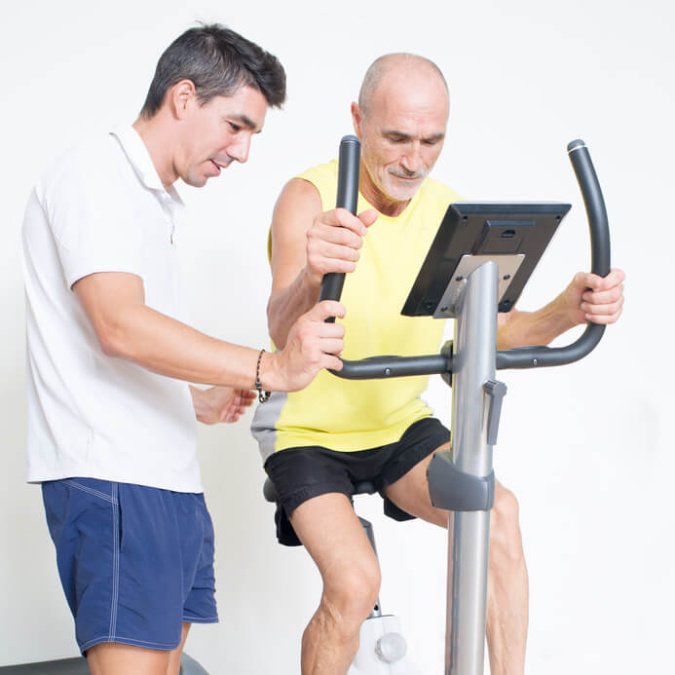 Ein Patient mit Rheuma macht unter Anleitung eines Therapeuten Sport auf einem Ergometer.