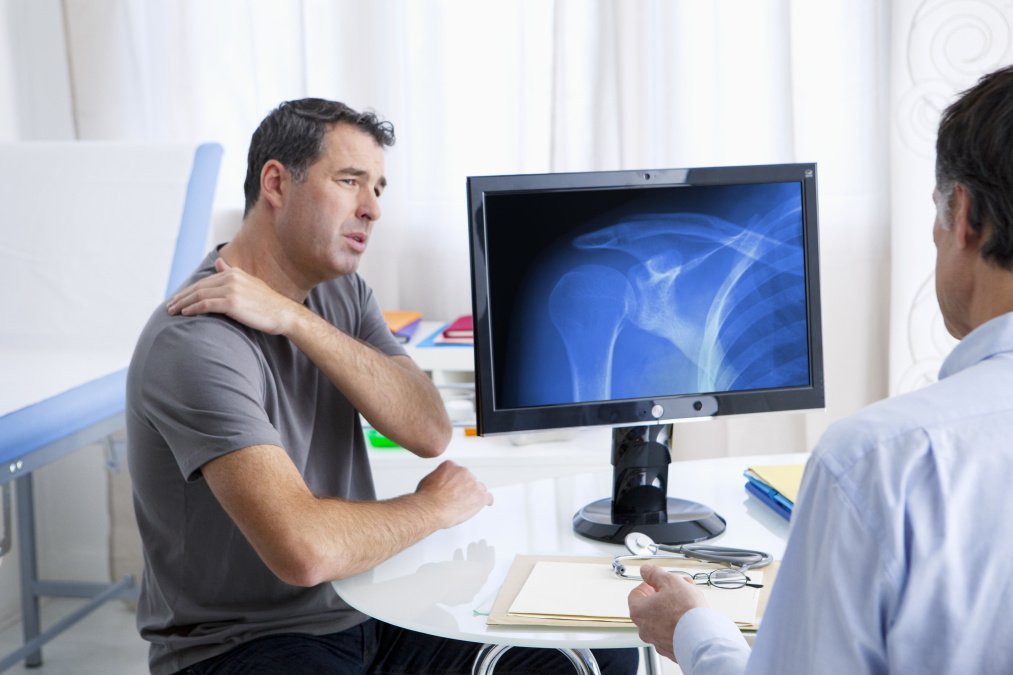 Arzt-Patienten-Gespräch, Patient hält schmerzende Schulter aufgrund eines Bruchs.