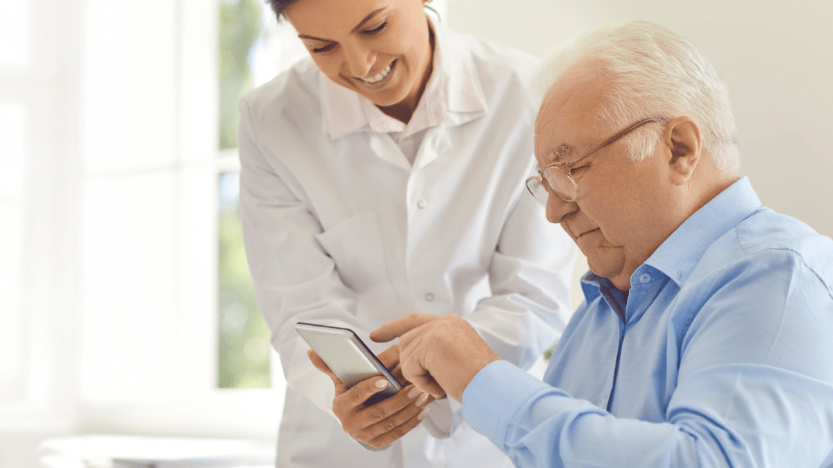 Ärztin unterstützt einen älteren Patienten bei der Nutzung einer Gesundheits-App.