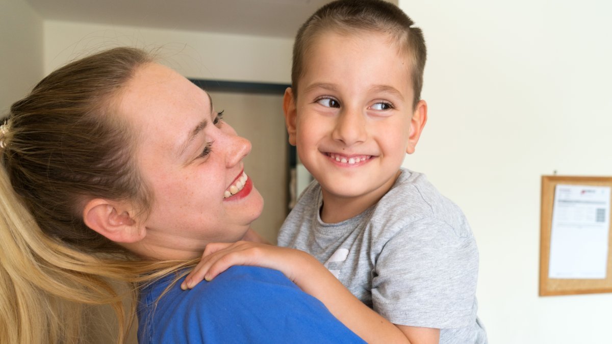 Pflegerin hält lächelnd einen kleinen Patienten im Arm – einfühlsame Betreuung in der VAMED Rehaklinik Altona