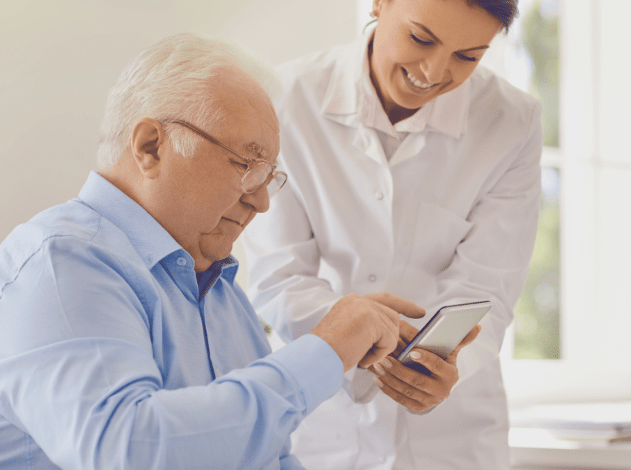 Sitzender Patient im blauen Hemd nutzt App während danebenstehende Ärztin die Anwendung erklärt