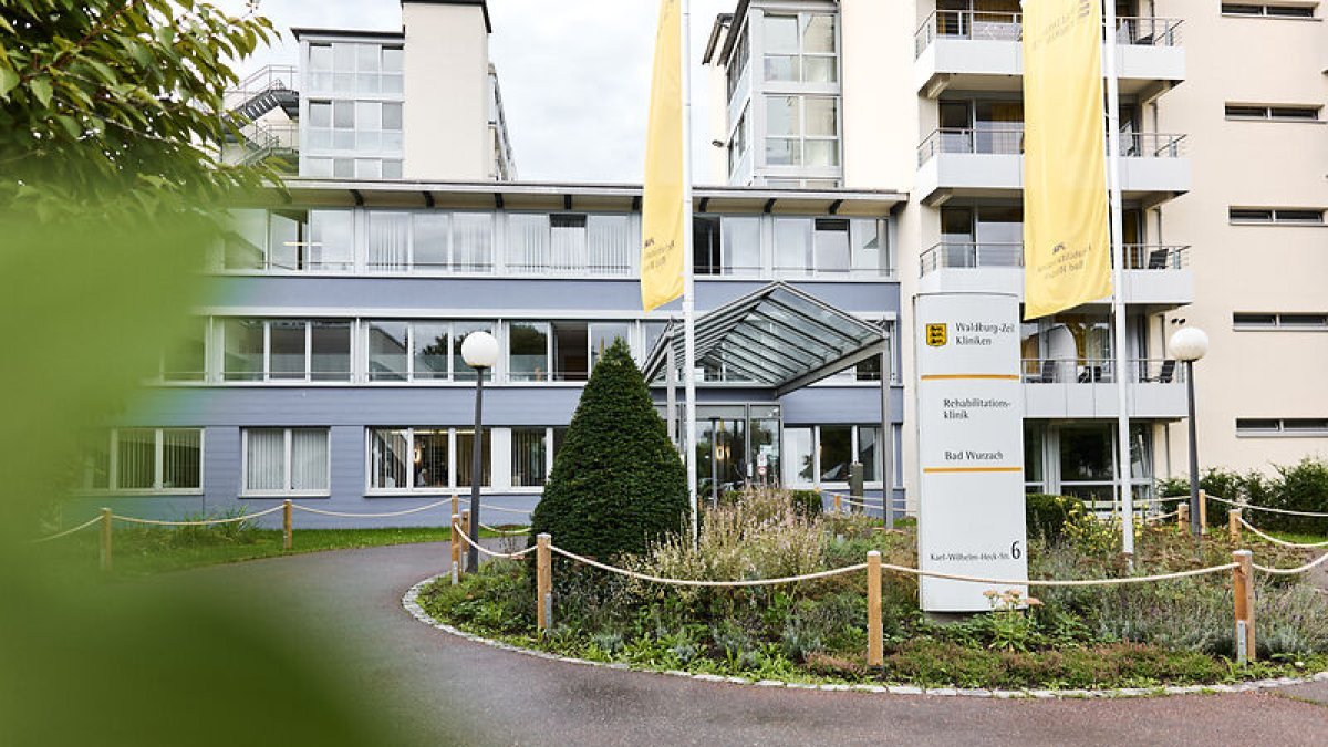 Außenansicht des Haupteingangs der Rehabilitationsklinik Bad Wurzach – moderne Architektur inmitten grüner Umgebung, mit gut erkennbarer Beschilderung und barrierefreiem Zugang.