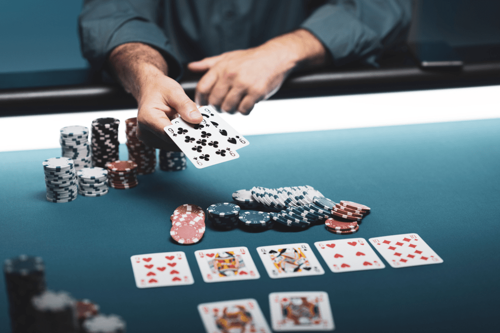 Ein Mann sitzt an einem Pokertisch mit Karten in der Hand und konzentriert sich auf das laufende Pokerspiel.