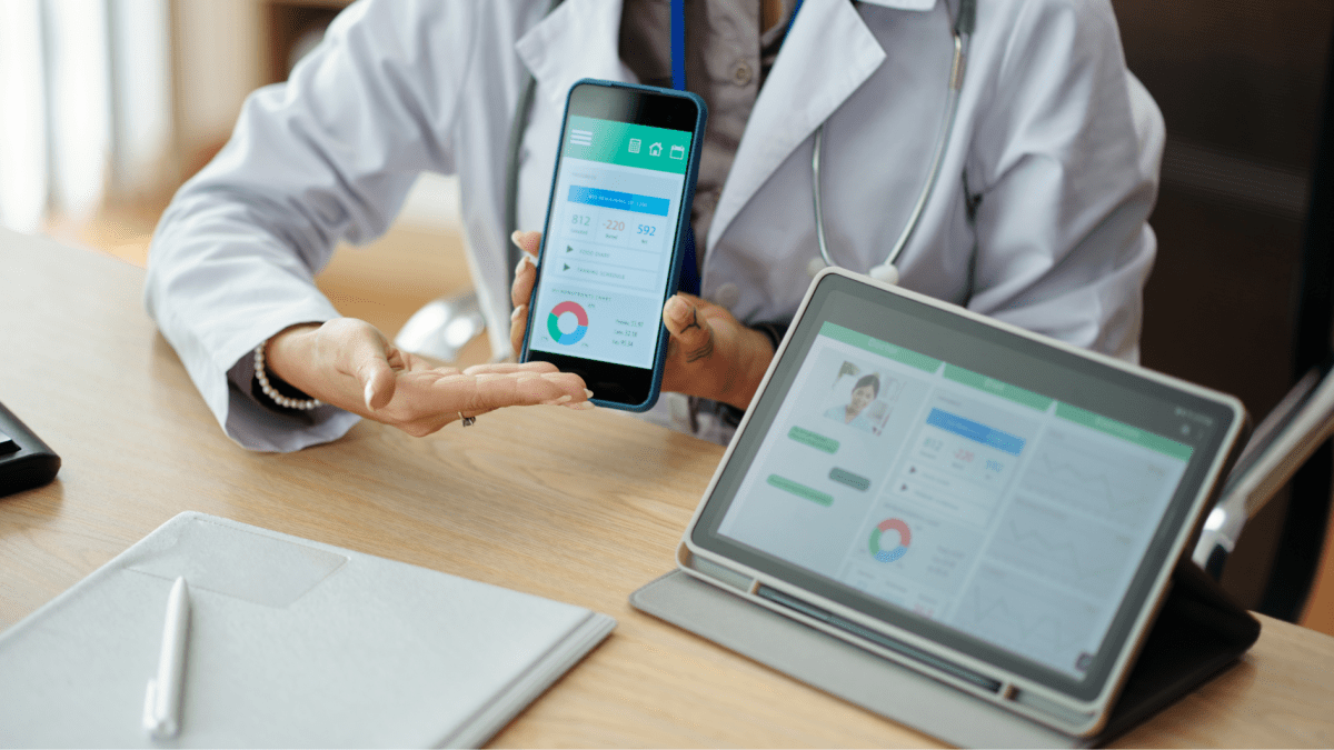 Eine medizinisches Fachperson, die ein Handy hält. Neben ihr ein Tablet. Darauf sind mehrere Grafiken und Kennzahlen zu sehen