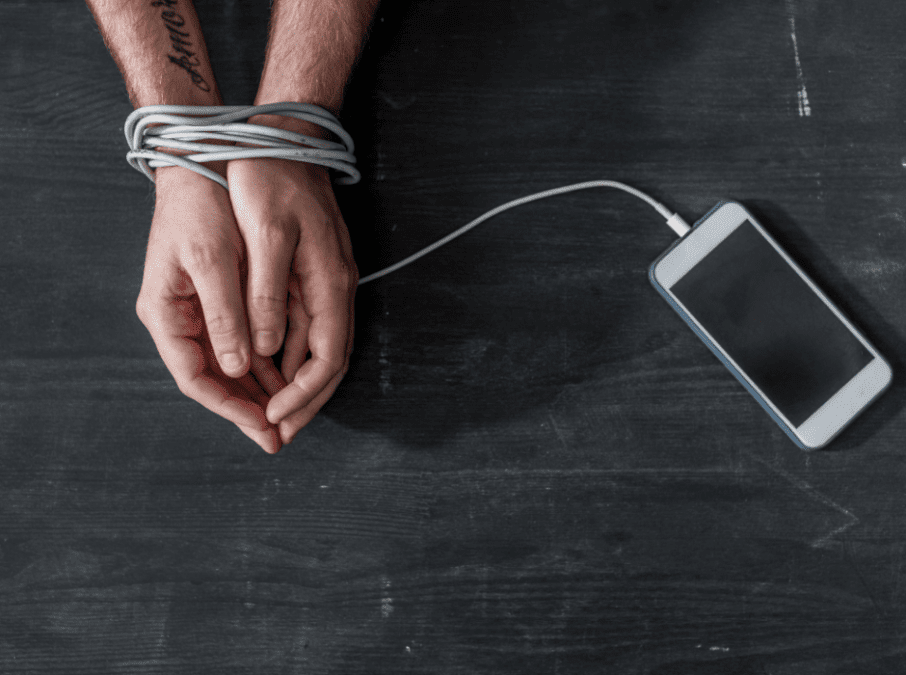 Hände eines Menschens sind mit dem Ladekabel des Handys zusammen gebunden.