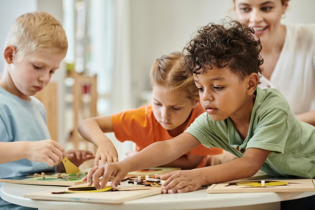 Kinder spielen gemeinsam während einer Reha, begleitet von einer Betreuungsperson.