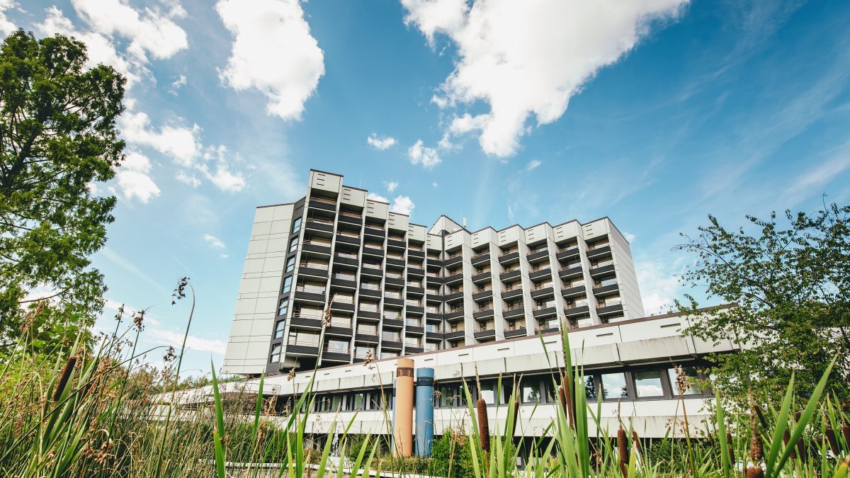 Gebäude der Klinik Roderbirken vor blauem Himmel umrahmt von Bäumen und Sträuchern
