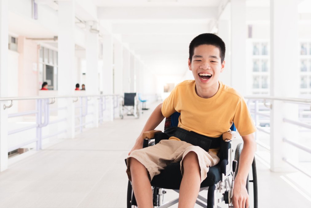 Ein lachendes Kind im Rollstuhl befindet sich in einem Krankenhaus und lebt mit Cerebralparese.